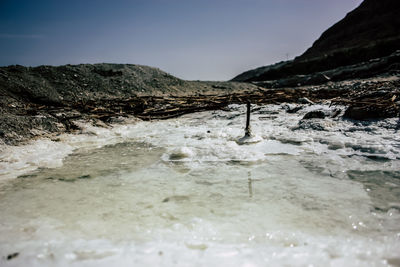 Surface level of water flowing through rocks against sky