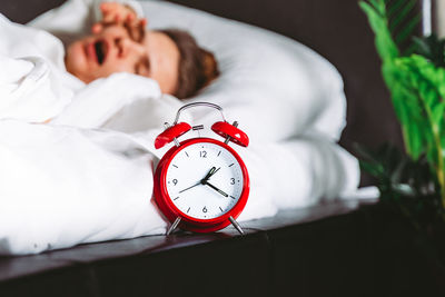 Sleepy young woman waking up in white bed yawning rubbing eyes turning off  alarm clock in bedroom.