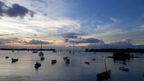 Sailboats moored on sea against sky at sunset