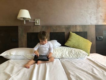 Full length of boy using digital tablet while sitting on bed at home