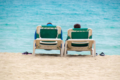 Rear view of people sitting on chair at beach