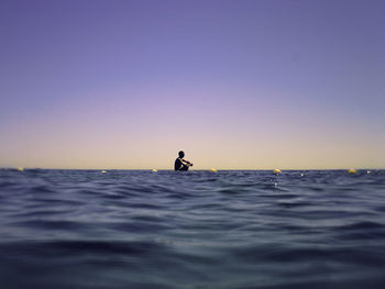 Man sitting in sea against clear sky