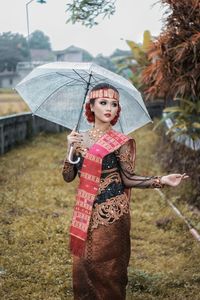 Portrait of woman with umbrella standing on field