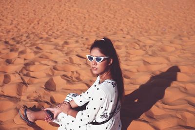 High angle view of woman wearing sunglasses lying on sand at beach