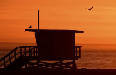 Silhouette lifeguard hut at beach against sky during sunset