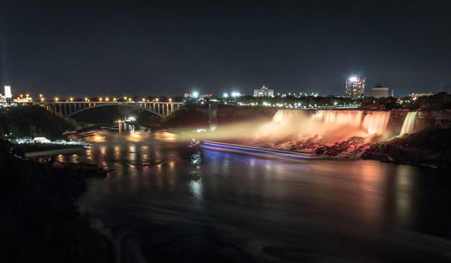 Illuminated bridge over river by buildings in city at night