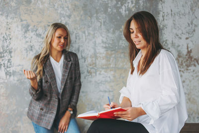 Businesswoman writing in diary while discussing with coworker in office