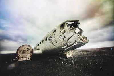 Abandoned airplane on beach against cloudy sky