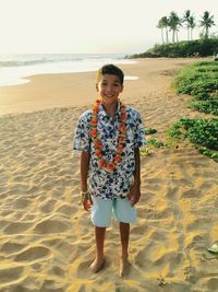 Portrait of cute smiling boy wearing floral garland on sandy beach