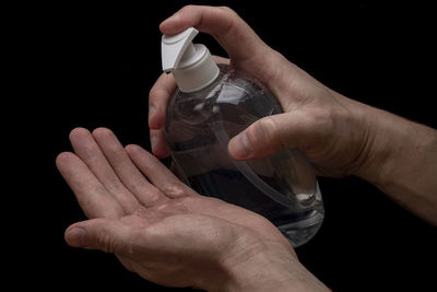 Midsection of person holding bottle against black background