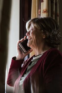 Side view of happy senior lady answering phone call while being at home