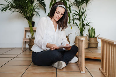 Woman holding papers while sitting on floor at home