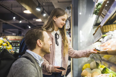 Cute daughter and father looking for fresh food on shelves in supermarket