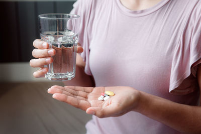 Midsection of woman holding glass of water and pills