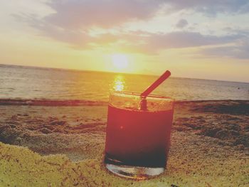 Close-up of drink on beach against sky during sunset