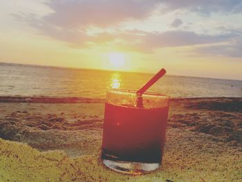 Close-up of drink on beach against sky during sunset