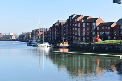 Sailboats moored on river by buildings against sky in city