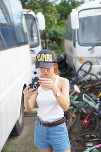Full length of boy holding camera while standing by car