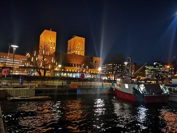 Illuminated buildings by river against sky at night