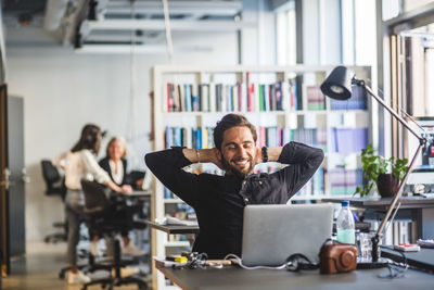 Businessman sitting with hands behind head at desk in office