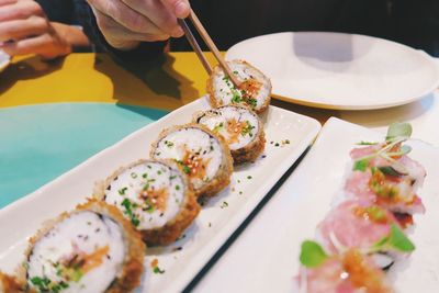 Cropped image of woman having sushi with chopsticks at table