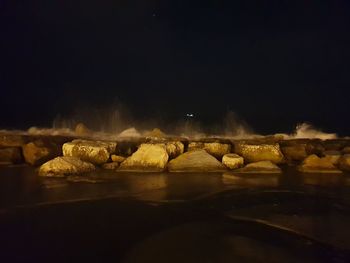 Rocks by sea against clear sky at night