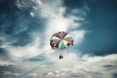 Low angle view of people paragliding against cloudy sky