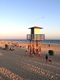 People on beach against clear sky during sunset