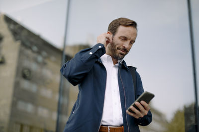 Low angle view of businessman using smart phone while standing against glass building