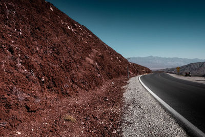 Road leading towards mountain against clear sky