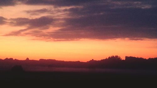 Silhouette of trees on landscape at sunset