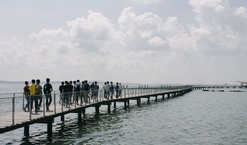 People walking on footbridge over sea against sky