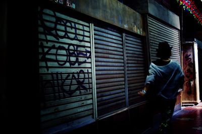 Rear view of man walking by illuminated store
