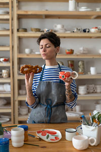 Female ceramic artist eating sweet delicious freshly baked bun and drinking tea in pottery studio
