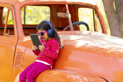 Girl using digital tablet and listening to music while leaning against abandoned car