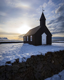 Church on snow by lake against sky during sunset