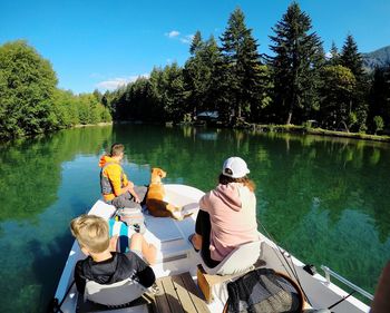 Rear view of people sitting on lake against trees