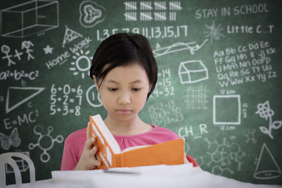 Girl studying at table against blackboard