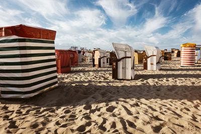 Hooded beach chairs on sand against sky