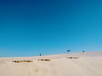Man walking on sand dune against clear blue sky