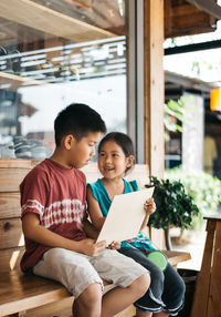 Siblings sitting with cardboard on bench