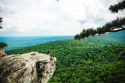 Man sitting on cliff against landscape and sky