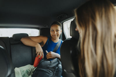 Blond female coach talking with teenage girl while sitting in car