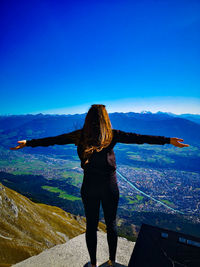 Rear view of woman with arms outstretched standing against mountain sky