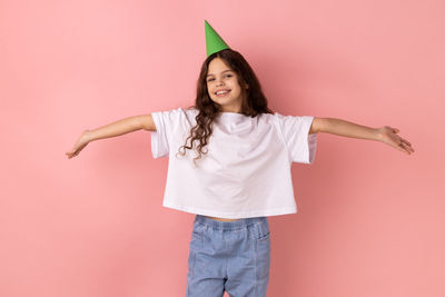 Portrait of young woman standing against pink background