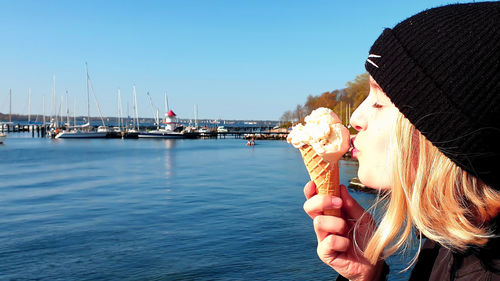 Close-up of girl kissing ice cream over sea against clear sky