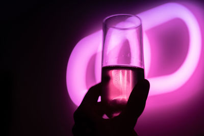 Close-up of hand holding glass against black and pink background