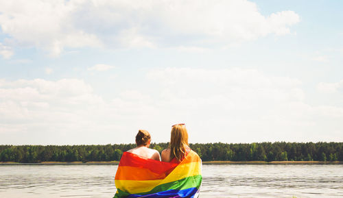 Couple sitting under rainbow pride flag at lake side