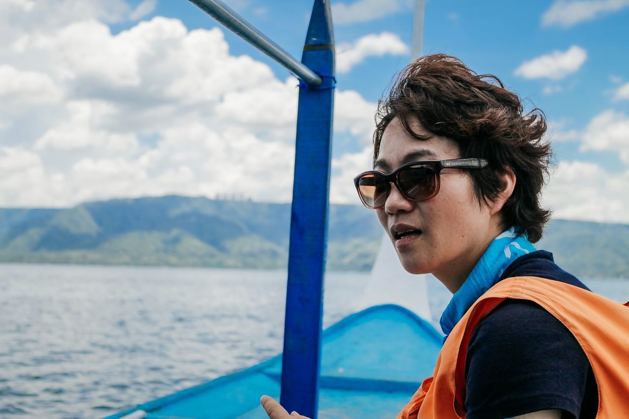 young adult, water, person, transportation, sky, lifestyles, mode of transport, leisure activity, sea, sunglasses, nautical vessel, travel, young women, boat, mountain, looking at camera, portrait, casual clothing