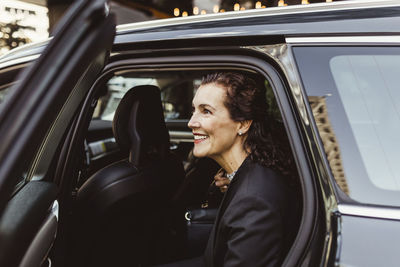Smiling female entrepreneur looking away while exiting from car